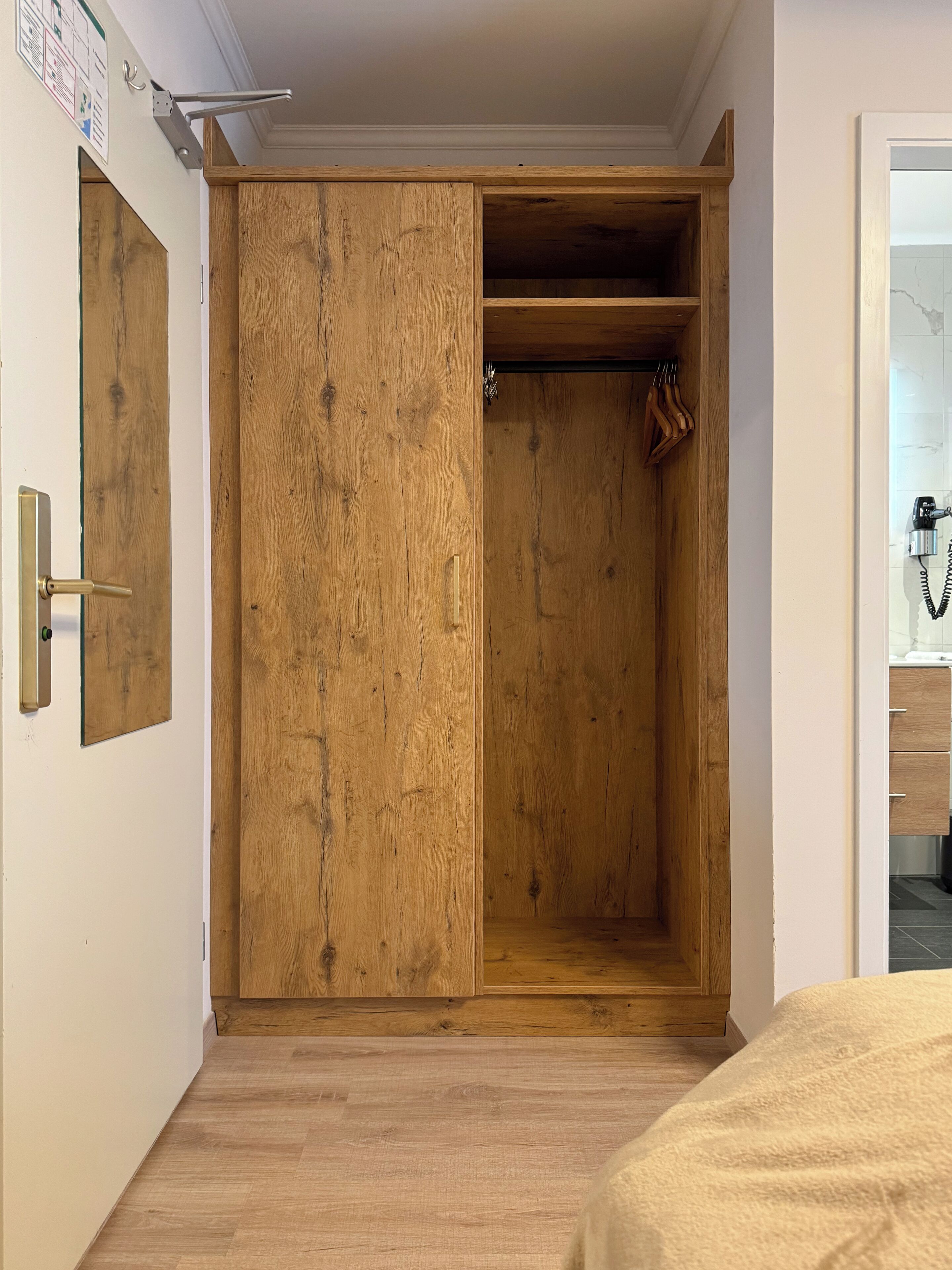 Un armario de madera con puerta corredera, un estante pequeño y una barra para colgar.