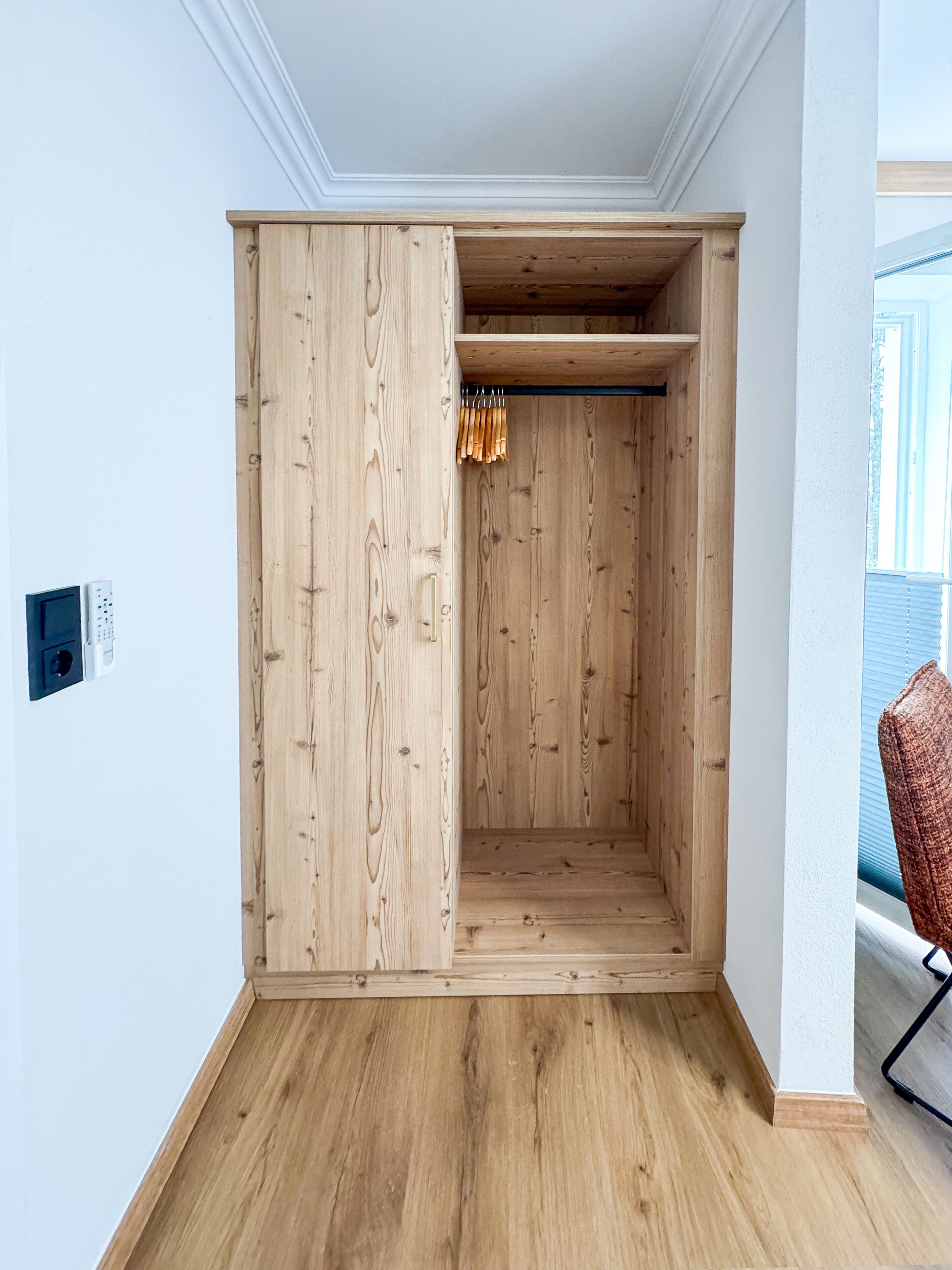 Een kamer met een houten garderobe, een klein plankje en een kledingroede.