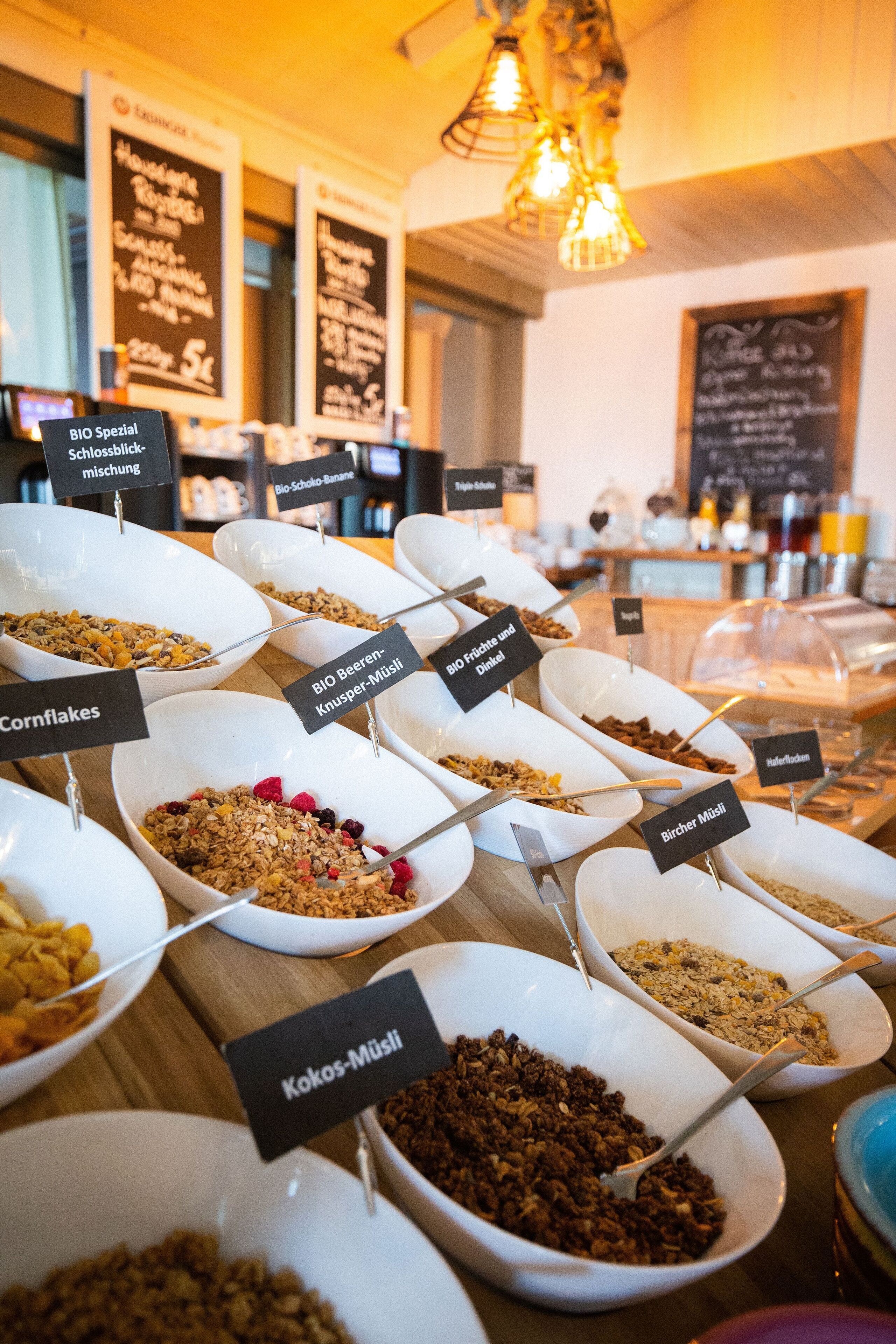 Een ontbijtbuffet met diverse bakken vol cornflakes en muesli, voorzien van labels.