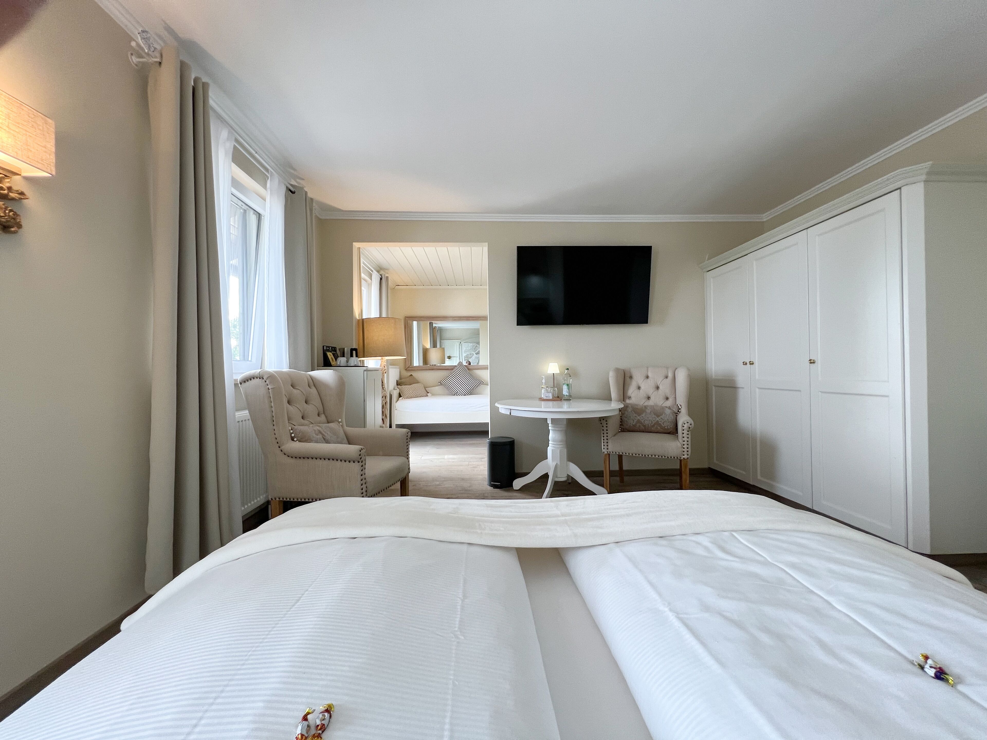 A hotel room with a bed, two armchairs, a small table, a TV, and a wardrobe.