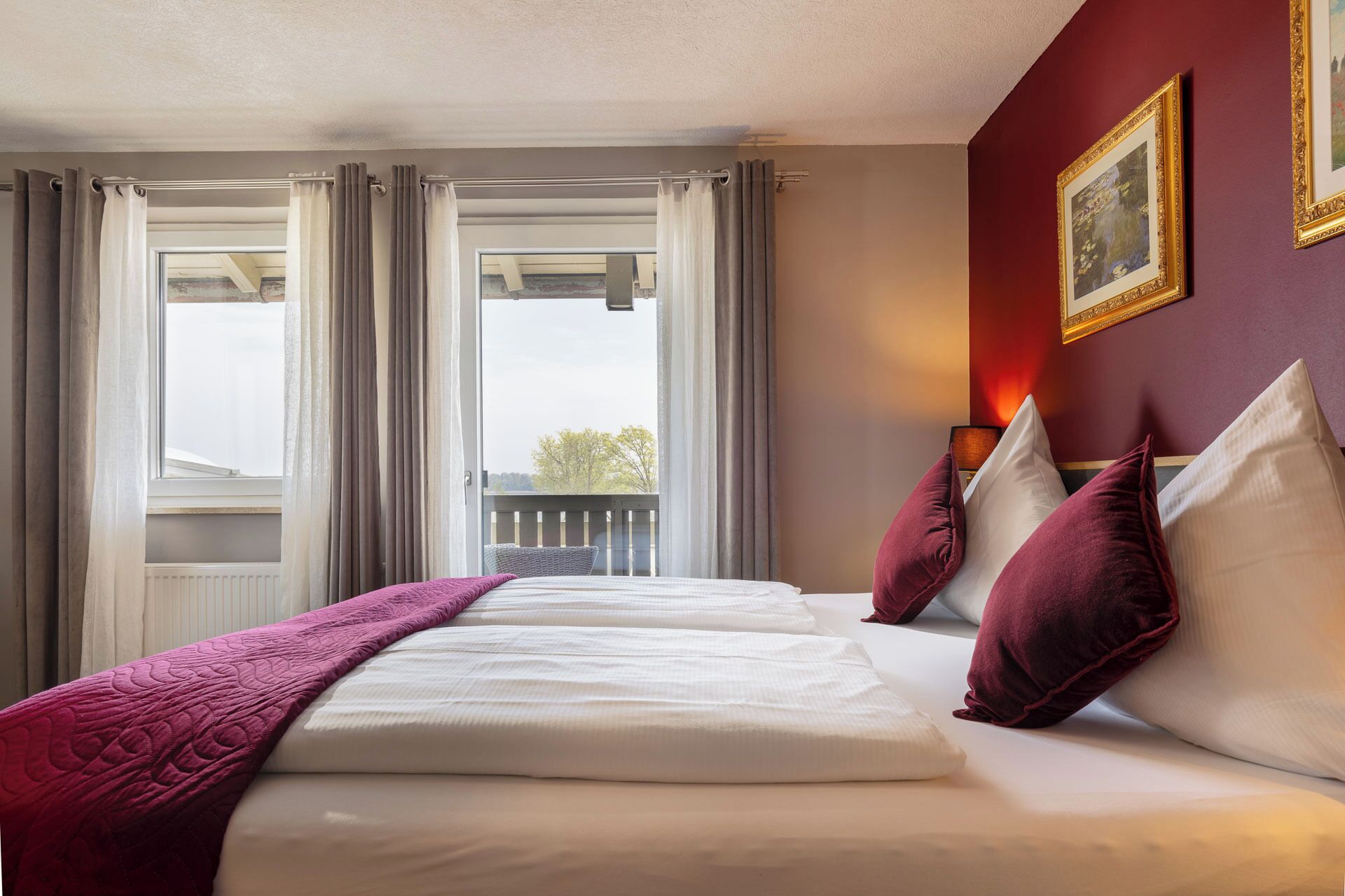 A hotel room with a large bed, two pillows, a blanket, and a window with curtains.
