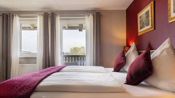 A hotel room with a large bed, two pillows, a blanket, and a window with curtains.