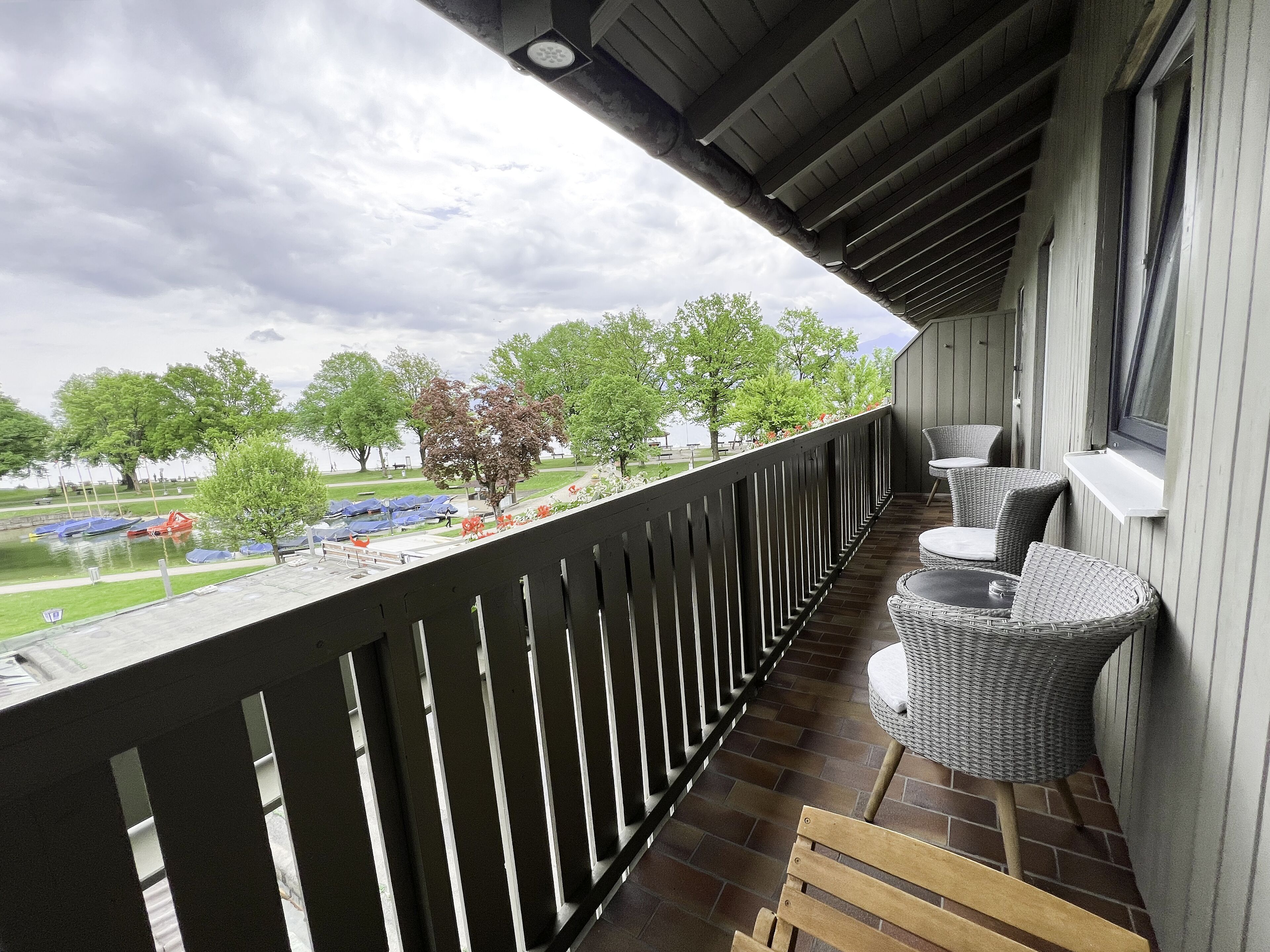 A balcony with wicker furniture, a view of a park, and a building with a sloped roof.