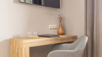 A modern room with a wooden desk, a grey upholstered chair, a flat-screen TV, and a vase with dried flowers.