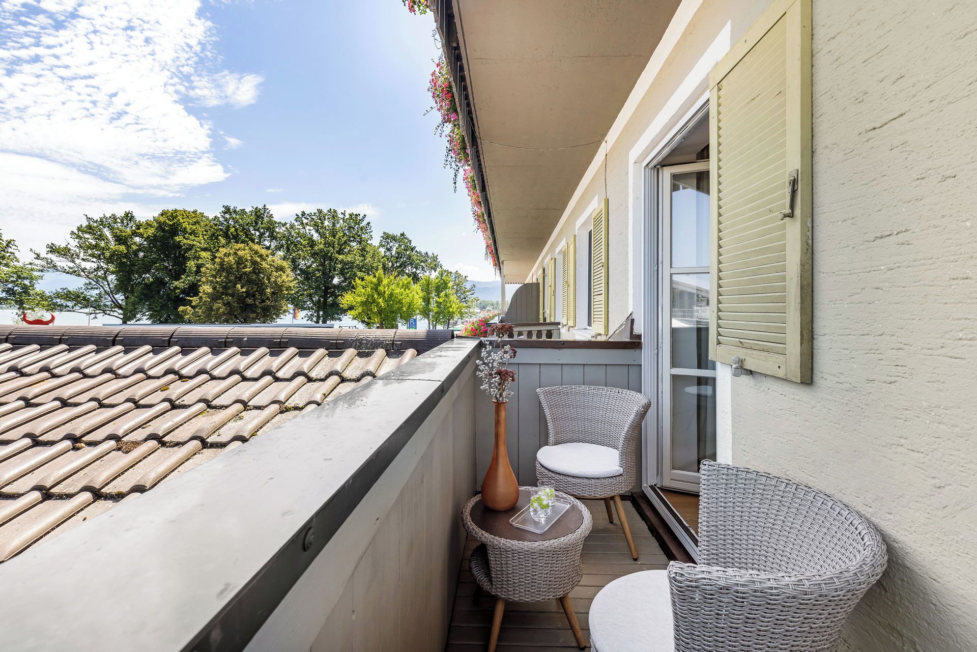 A balcony with a tiled roof, wicker chairs, a small table, and a vase with flowers.