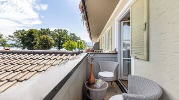 A balcony with a tiled roof, wicker chairs, a small table, and a vase with flowers.