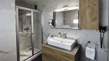 A modern bathroom with a glass-enclosed shower, a wooden vanity, and a marble-tiled wall.