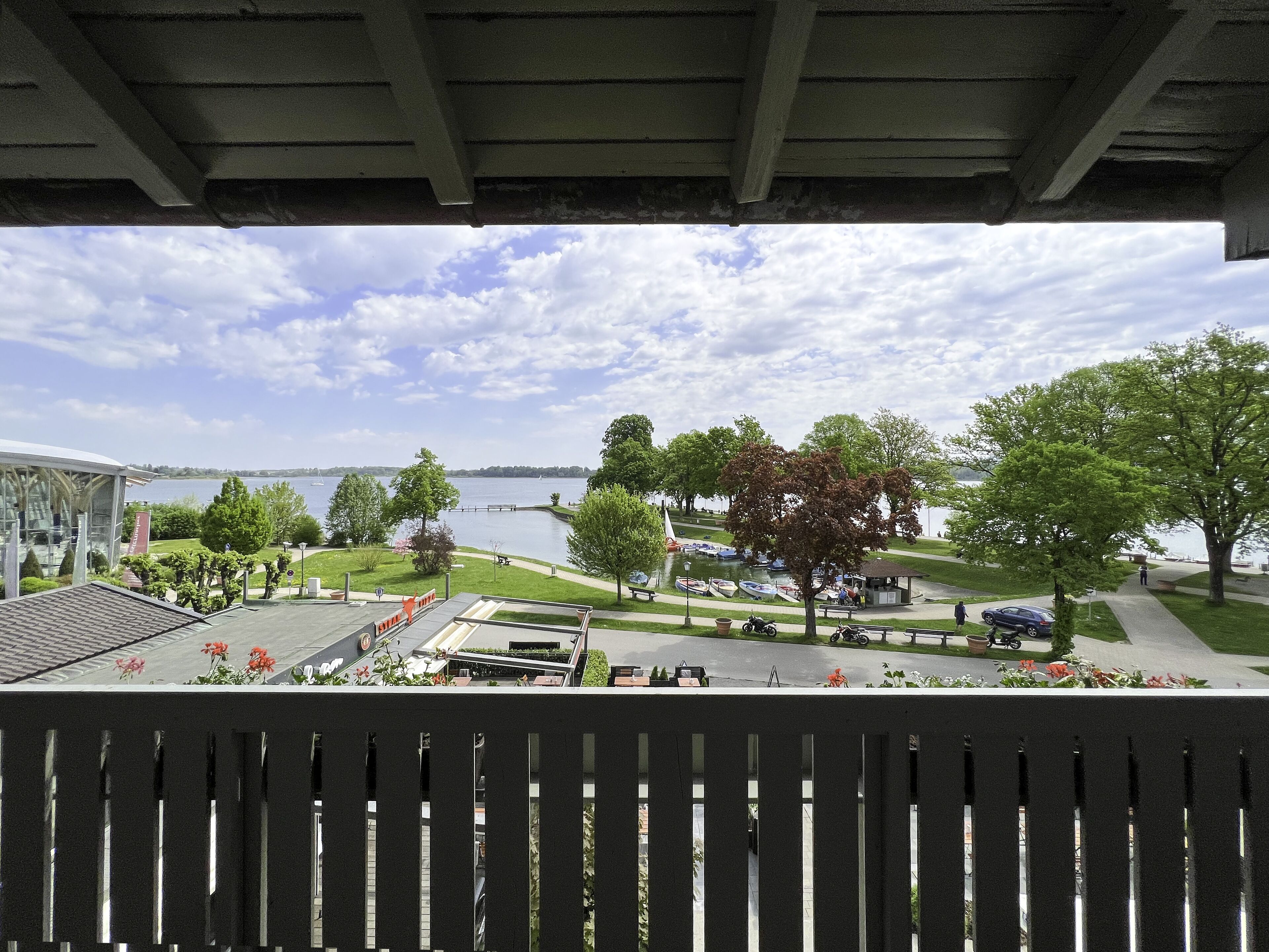 Blick vom Balkon auf einen Park mit einem See, Booten und einem Gazebo.