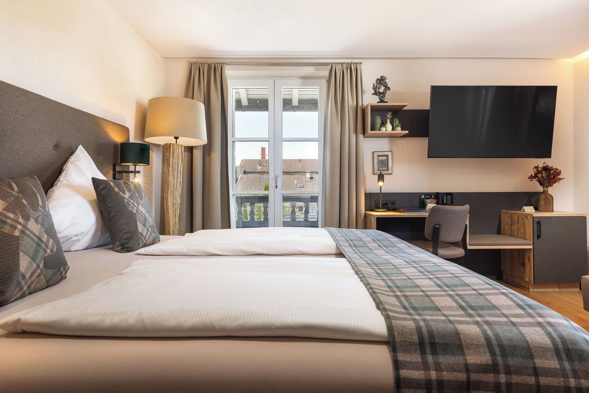 Habitación de hotel con cama, escritorio, silla, televisor y vistas al exterior.
