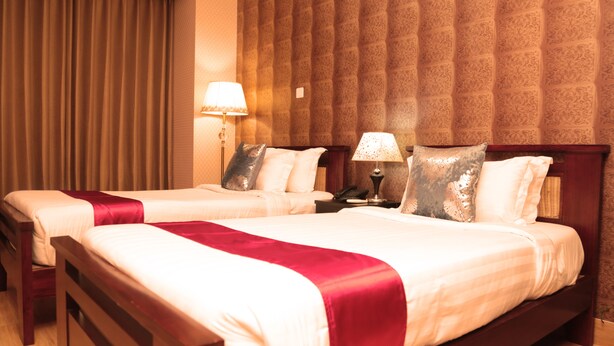 A hotel room with two beds, each with a red and white bedspread, a wooden headboard, and a nightstand with a lamp.