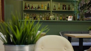 Zona de bar con estantes llenos de botellas de licor, una planta en maceta y un área de estar con una mesa y sillas.