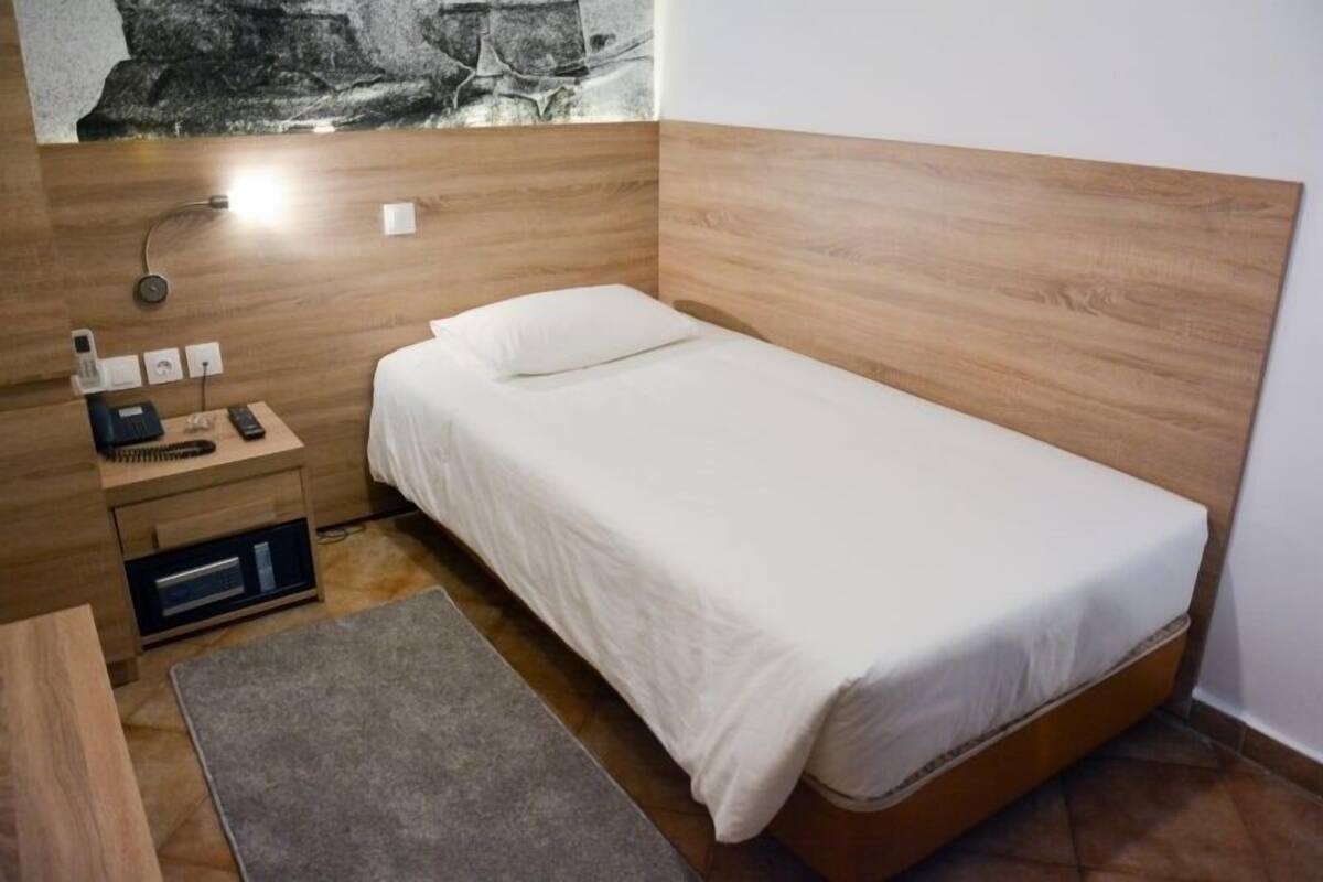 Ein kleines, modernes Schlafzimmer mit einem Holzkopfende, einem Einzelbett, einem Nachttisch mit Lampe, Telefon und einer kleinen Schublade.
