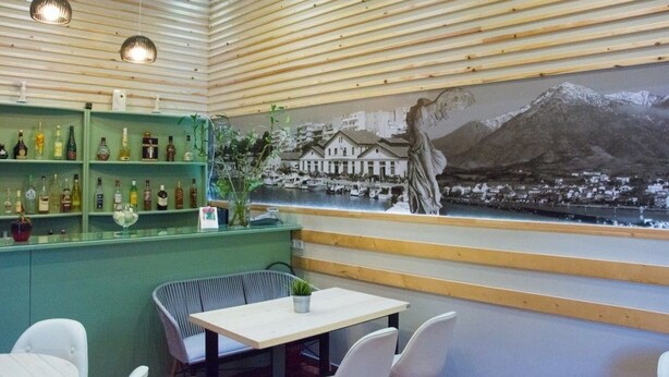Un restaurante con una zona de bar verde, sillas blancas y un mural de una ciudad costera.
