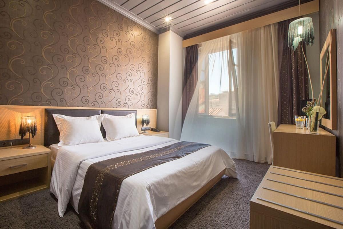 A hotel room with a large bed, bedside tables, a desk, and a mirror.