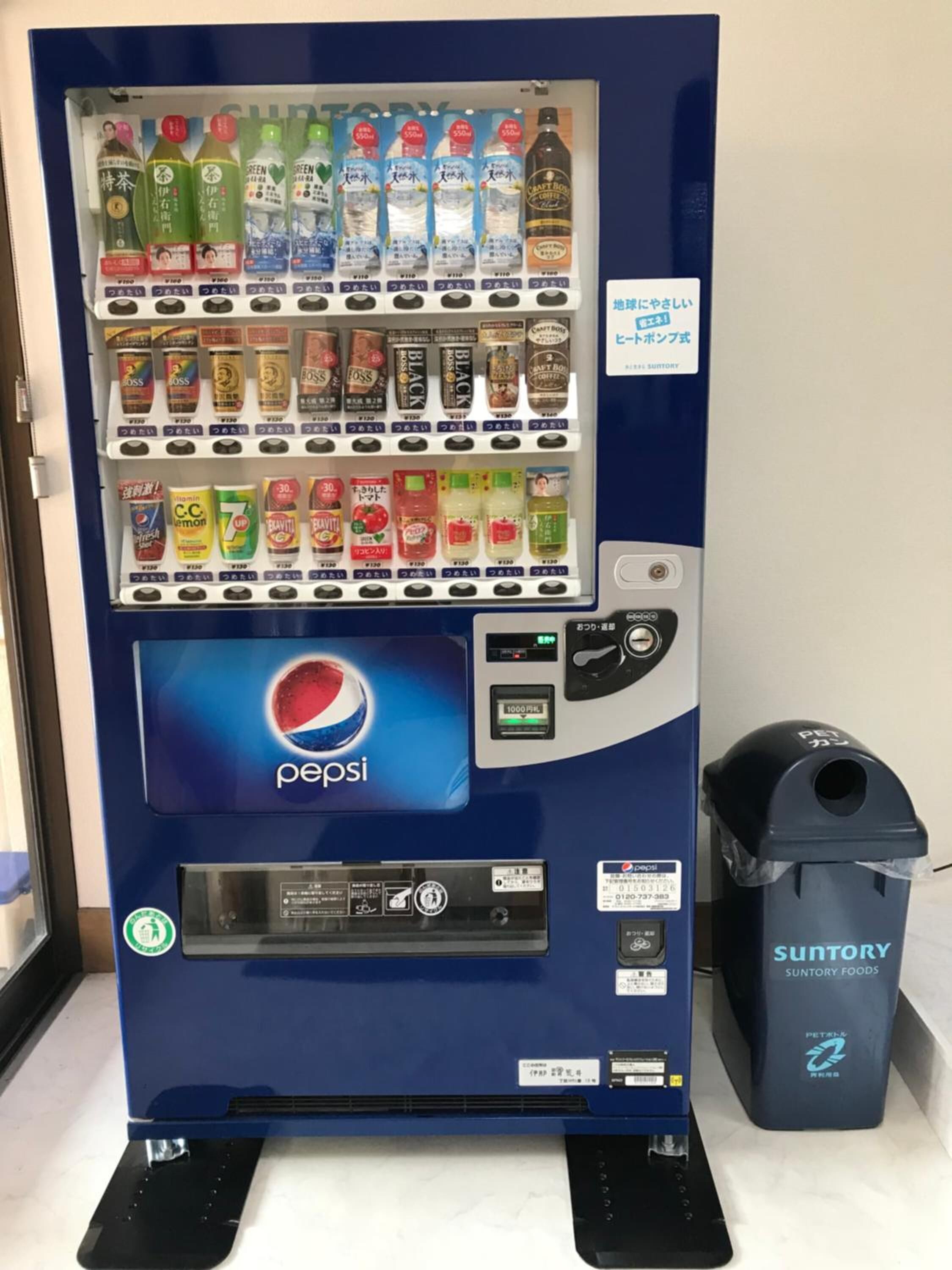 Máquina expendedora con el logo de Pepsi, diversas bebidas y un basurero etiquetado como 'Suntory'.