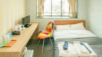 A hotel room with a bed, a desk with a computer, a chair, and a window with curtains.