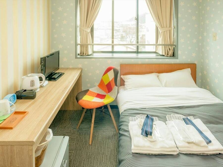Habitación de hotel con cama, escritorio con ordenador, silla y ventana con cortinas.