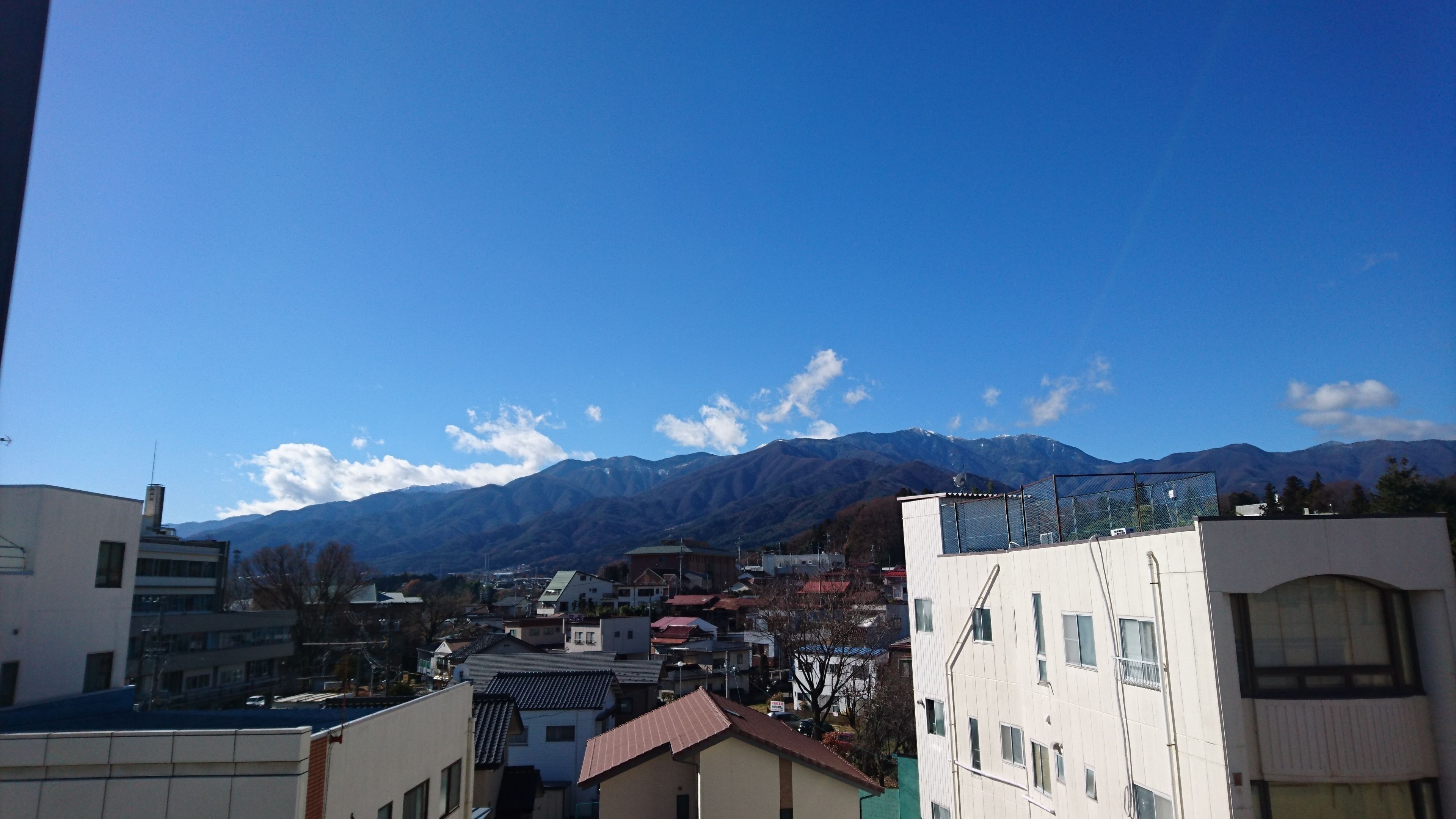 A residential area with buildings, a clear sky, and mountains in the background.