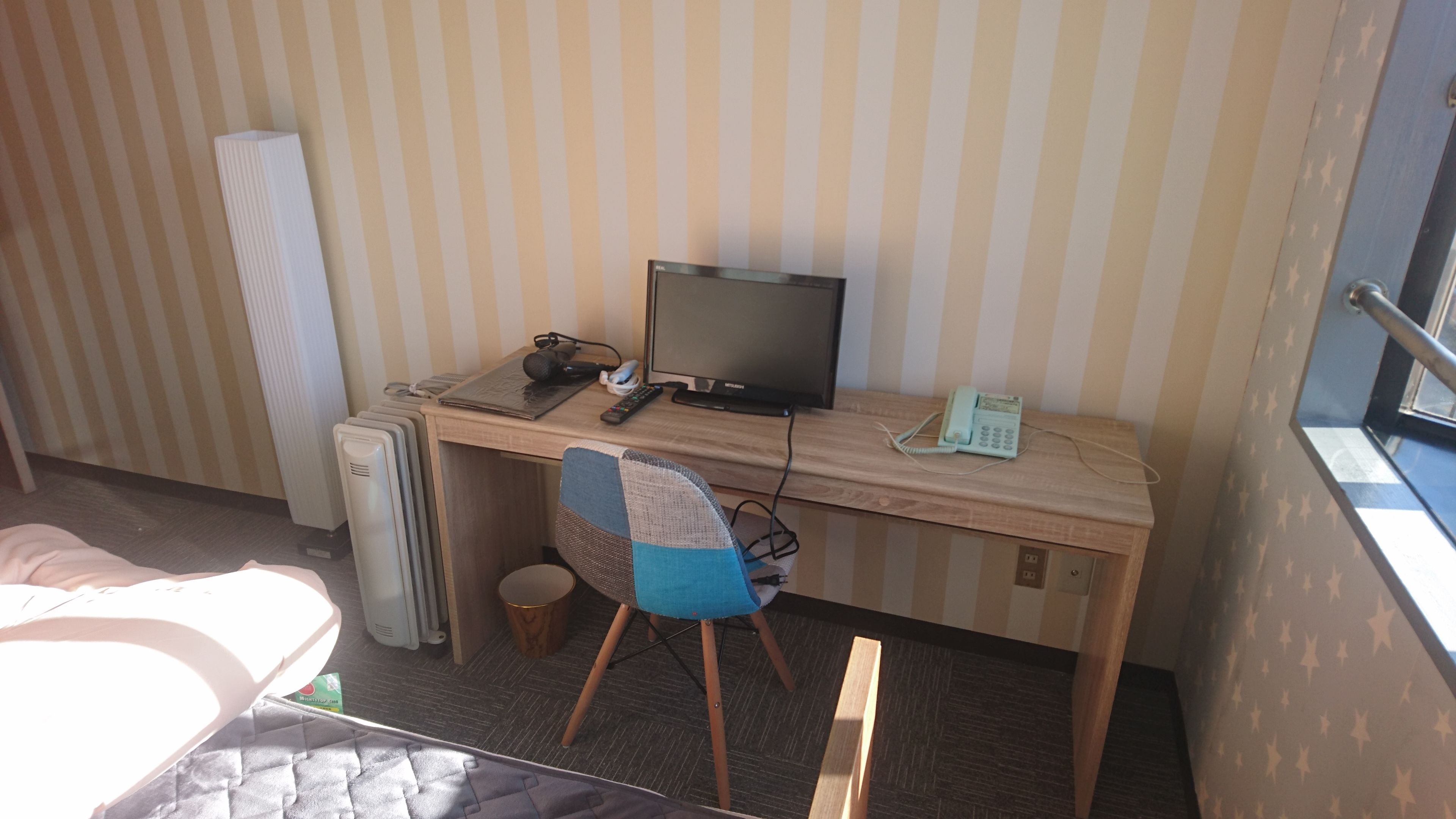 Una habitación pequeña y acogedora con un escritorio de madera, una computadora, una silla, un radiador y una ventana con cortina estampada de estrellas.