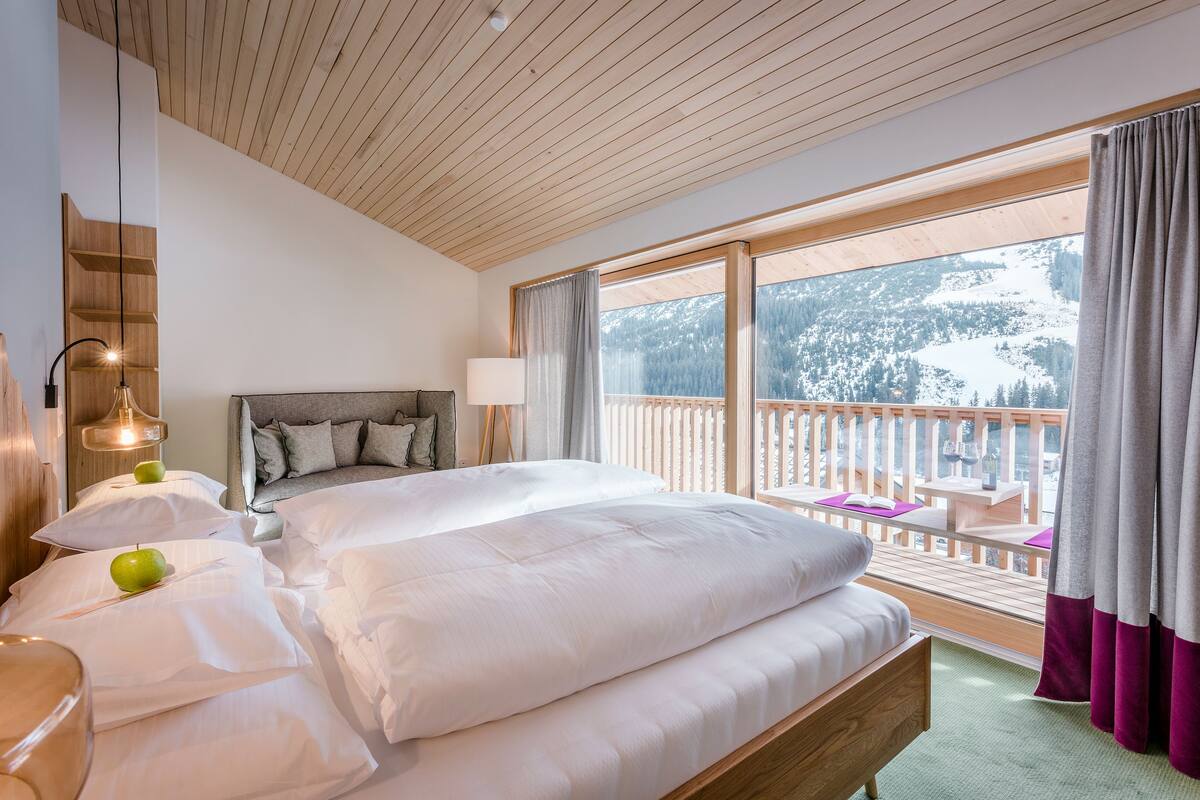 Un dormitorio espacioso con una cama grande, cabecera de madera y un balcón con vista a una montaña nevada.