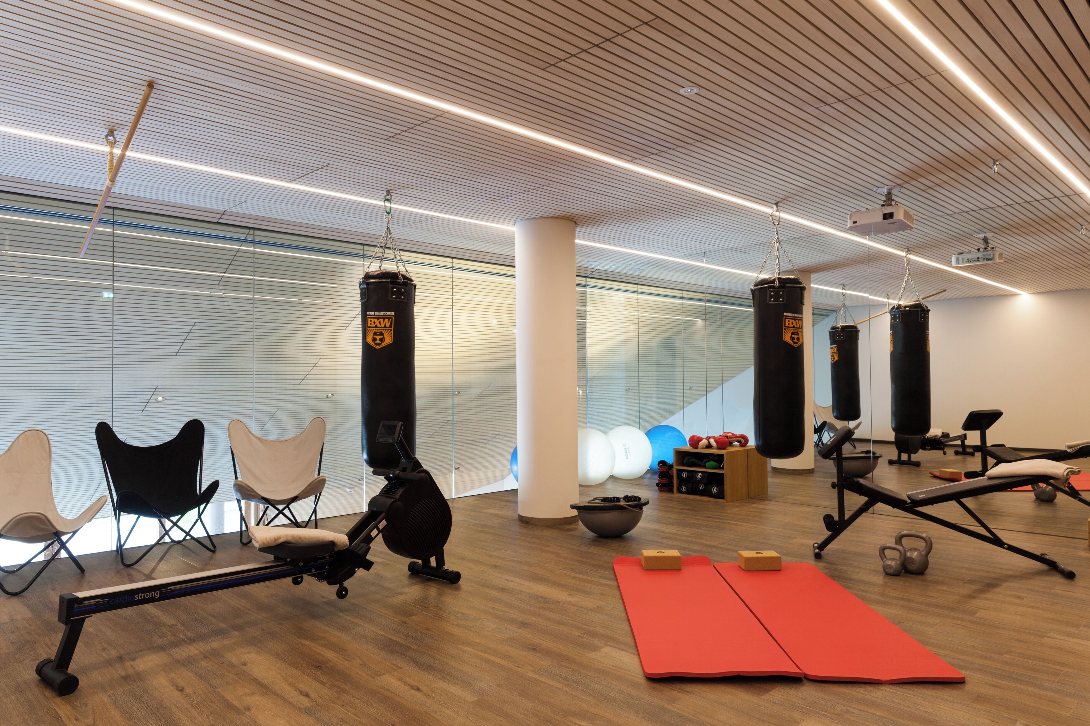 A modern gym with exercise equipment, punching bags, and a wooden floor.