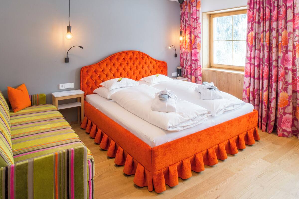 Una habitación de hotel con una cama grande, una mesita de noche, una lámpara y una ventana con cortinas.