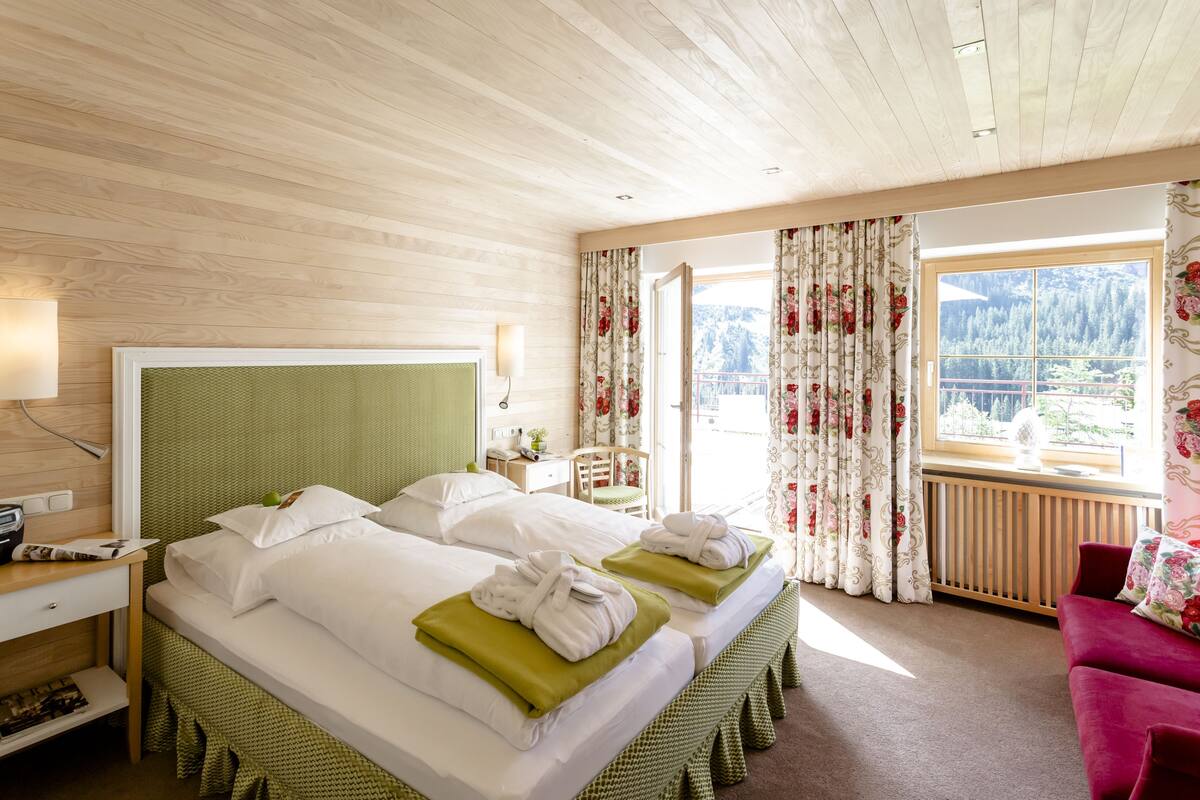 Habitación de hotel con dos camas, un escritorio, una silla y vistas a un paisaje montañoso.