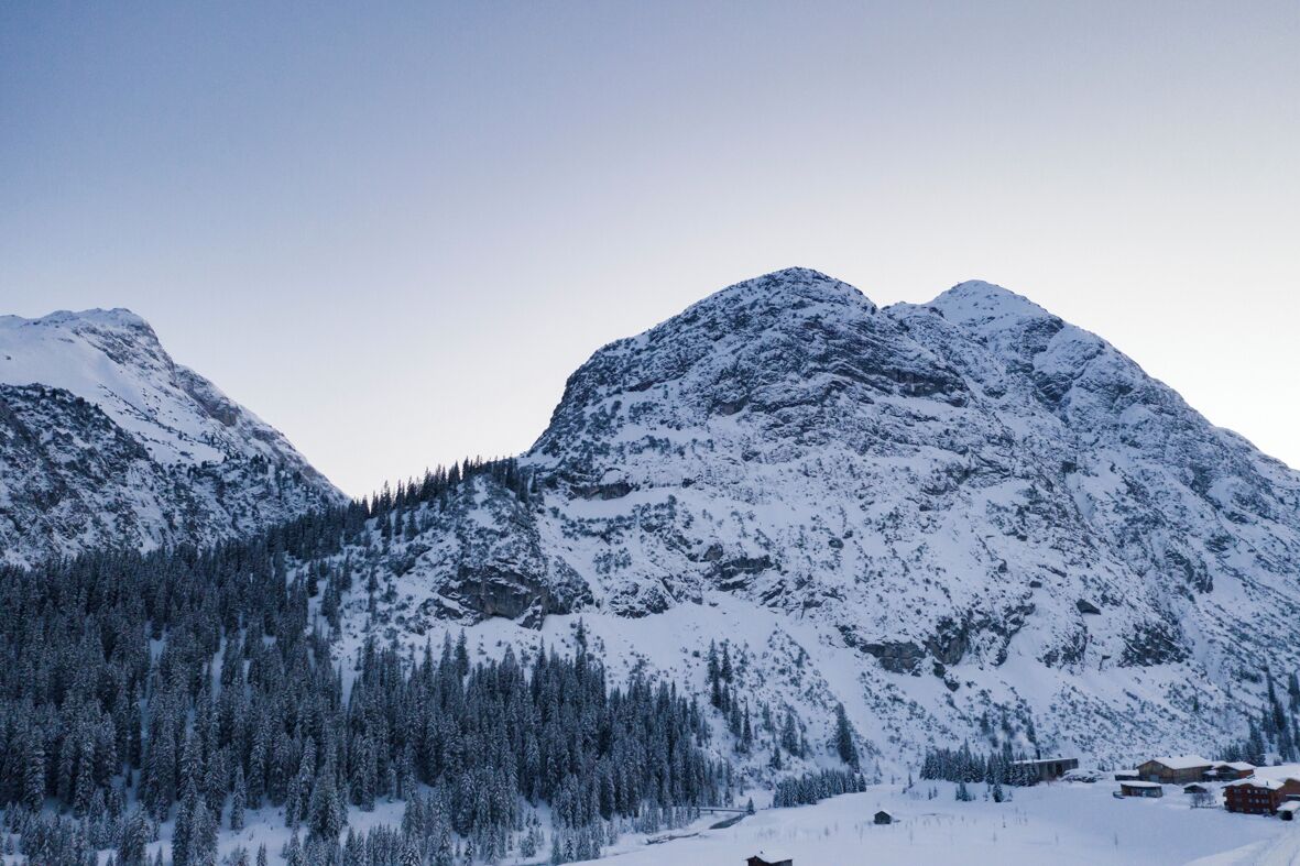 Un paisaje montañoso con picos nevados y un valle cubierto de bosque.