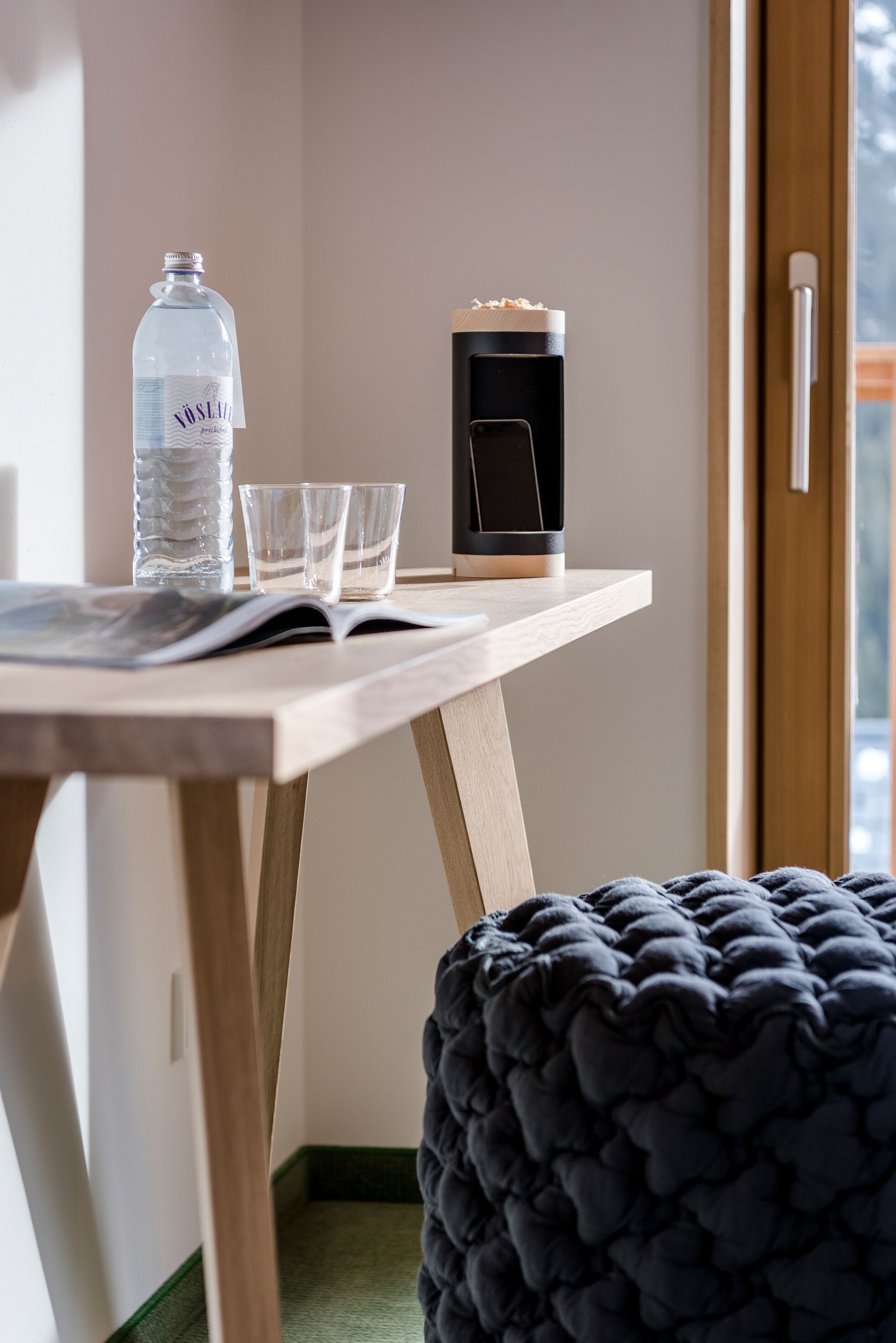 Une table en bois avec une bouteille d’eau, deux verres, un téléphone intelligent et un magazine ouvert.