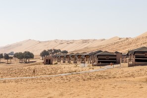 A desert resort with multiple tents arranged in rows, a paved pathway, and sparse vegetation.