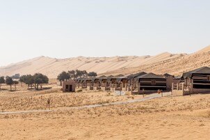Un resort en el desierto con varias tiendas dispuestas en filas, un camino pavimentado y vegetación escasa.