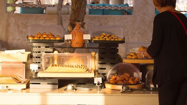 En buffet med forskellige retter, blandt andet kager og brød, præsenteret i gennemsigtige beholdere.