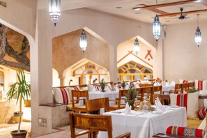 A restaurant with wooden chairs and tables, hanging lanterns, and a mural on the wall. - Thousand Nights-Ash Sharqiyah Sands (Bidiya)