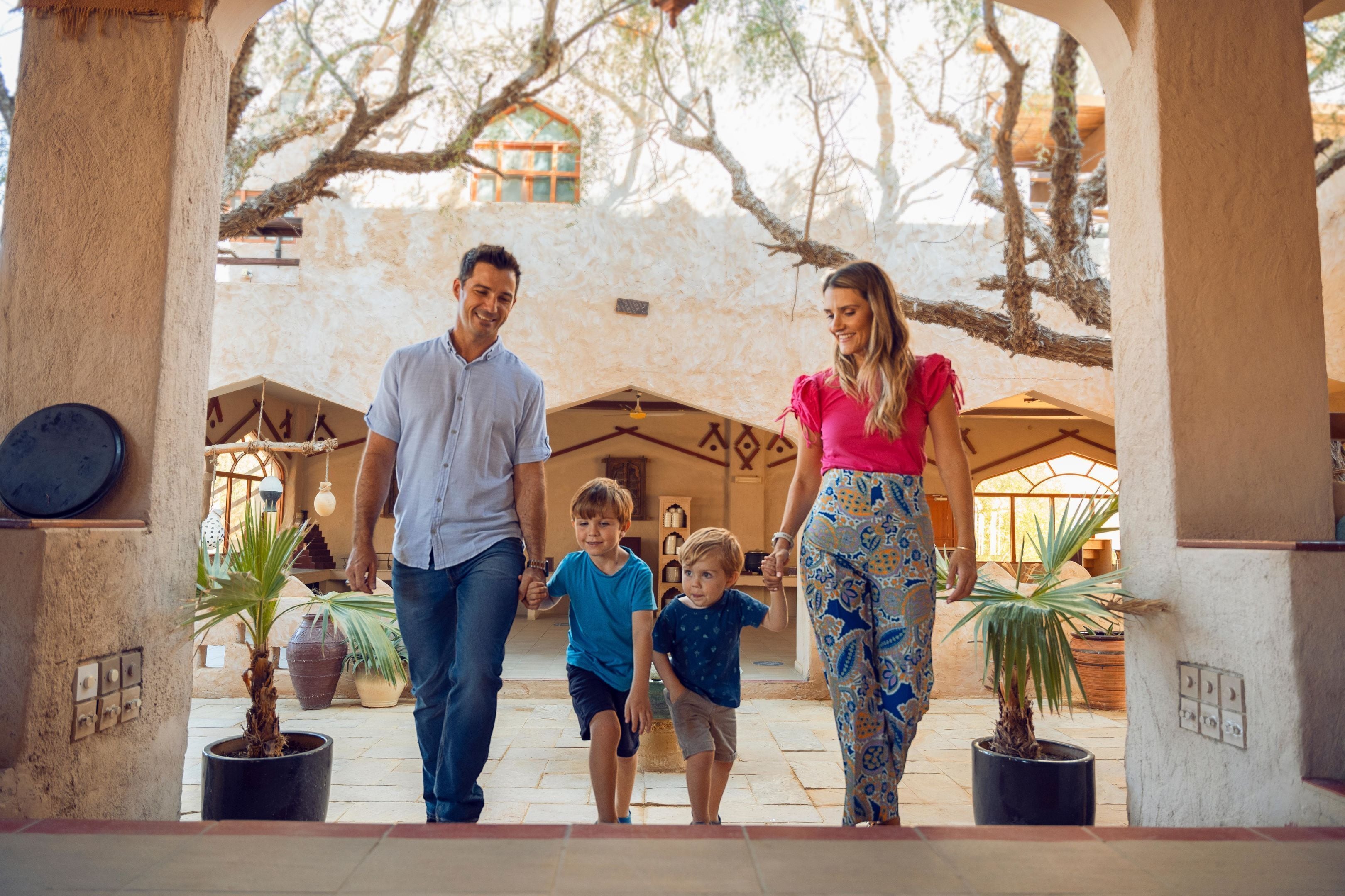Une famille se promène dans une cour intérieure agrémentée de plantes en pot et d’arches architecturales.