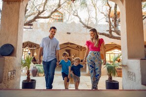 A family walking through a courtyard with potted plants and architectural arches. - Thousand Nights-Ash Sharqiyah Sands (Bidiya)