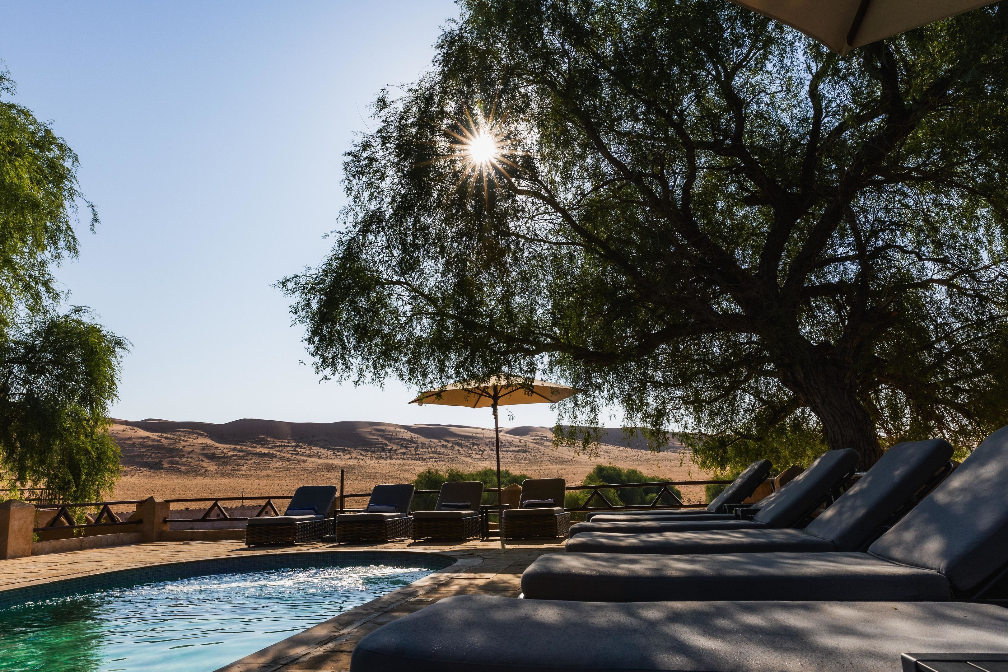 A poolside area with lounge chairs and an umbrella, overlooking a hilly landscape.