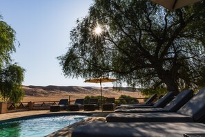 Zona de piscina amb gandules i una ombrel·la, amb vista a un paisatge amb turons.