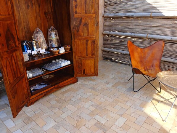 A wooden cabinet with shelves containing jars, a chair, and a table.