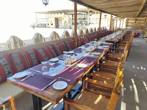 A long dining table set with chairs, a view of the sea, and a covered outdoor seating area. - Thousand Nights-Ash Sharqiyah Sands (Bidiya)