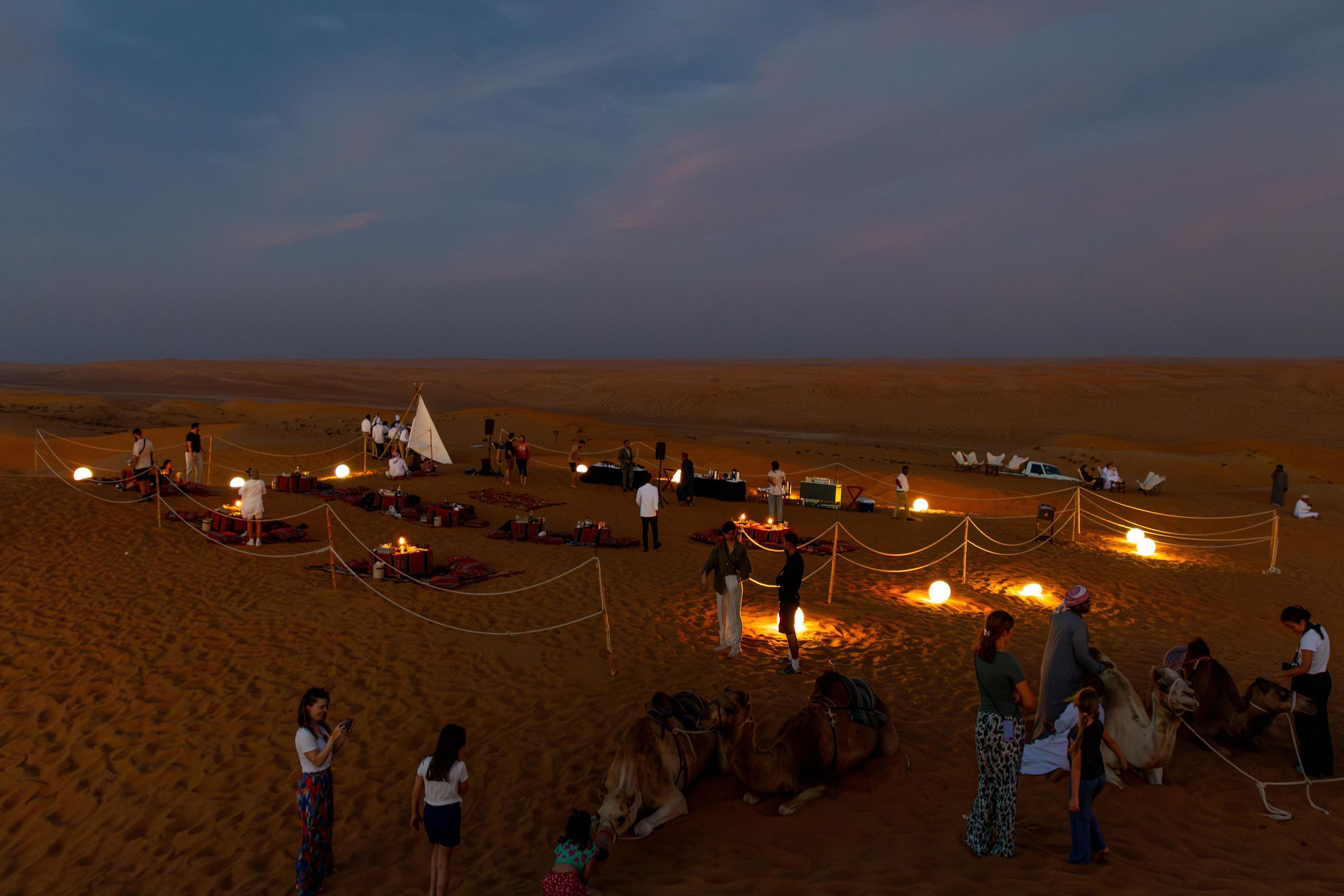 A desert campsite with tents, camels, and people.
