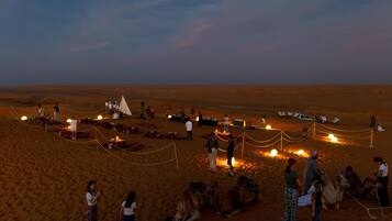 A desert campsite with tents, camels, and people.