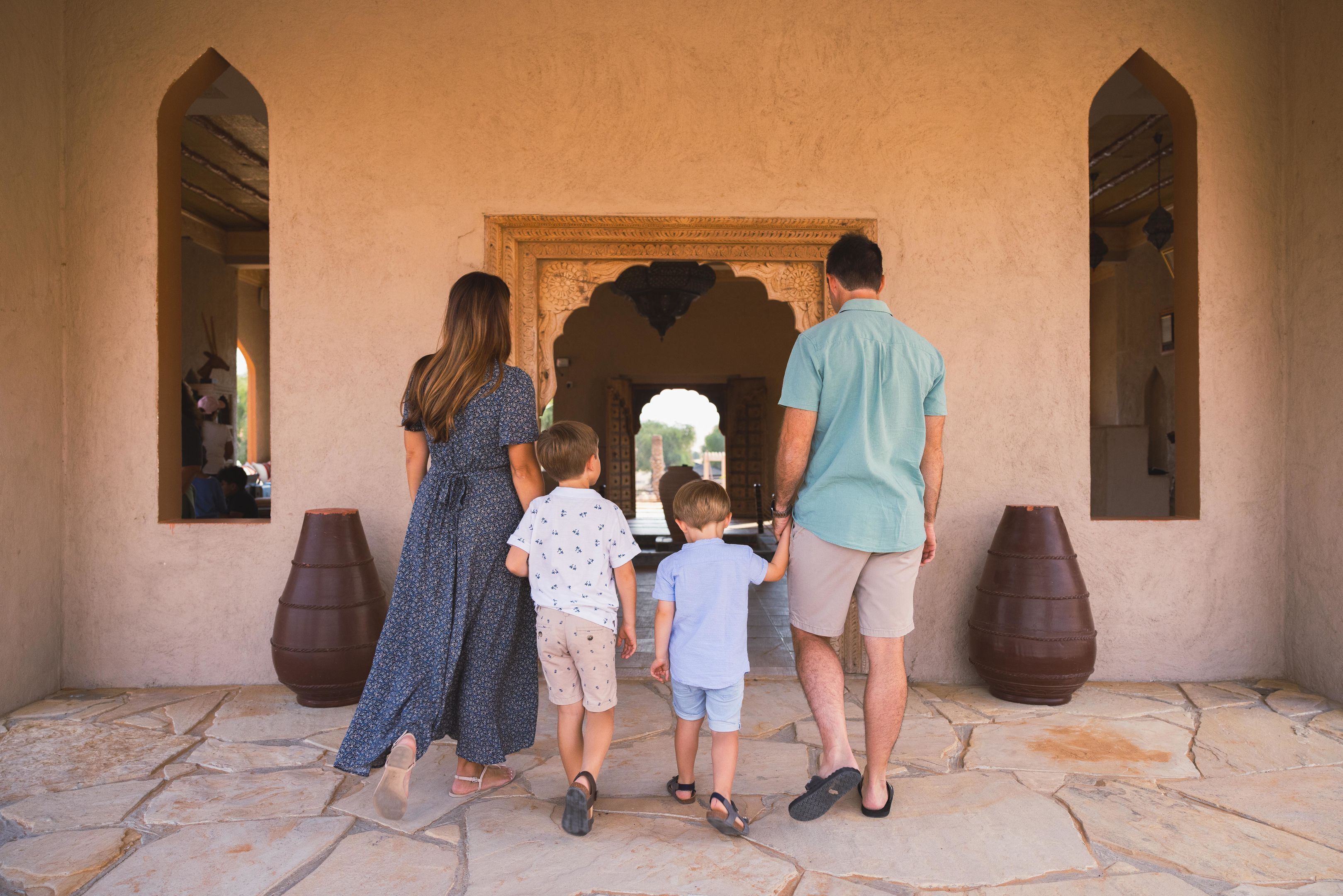 A family of four walking through an arched doorway in a building with stone flooring and large wooden barrels.