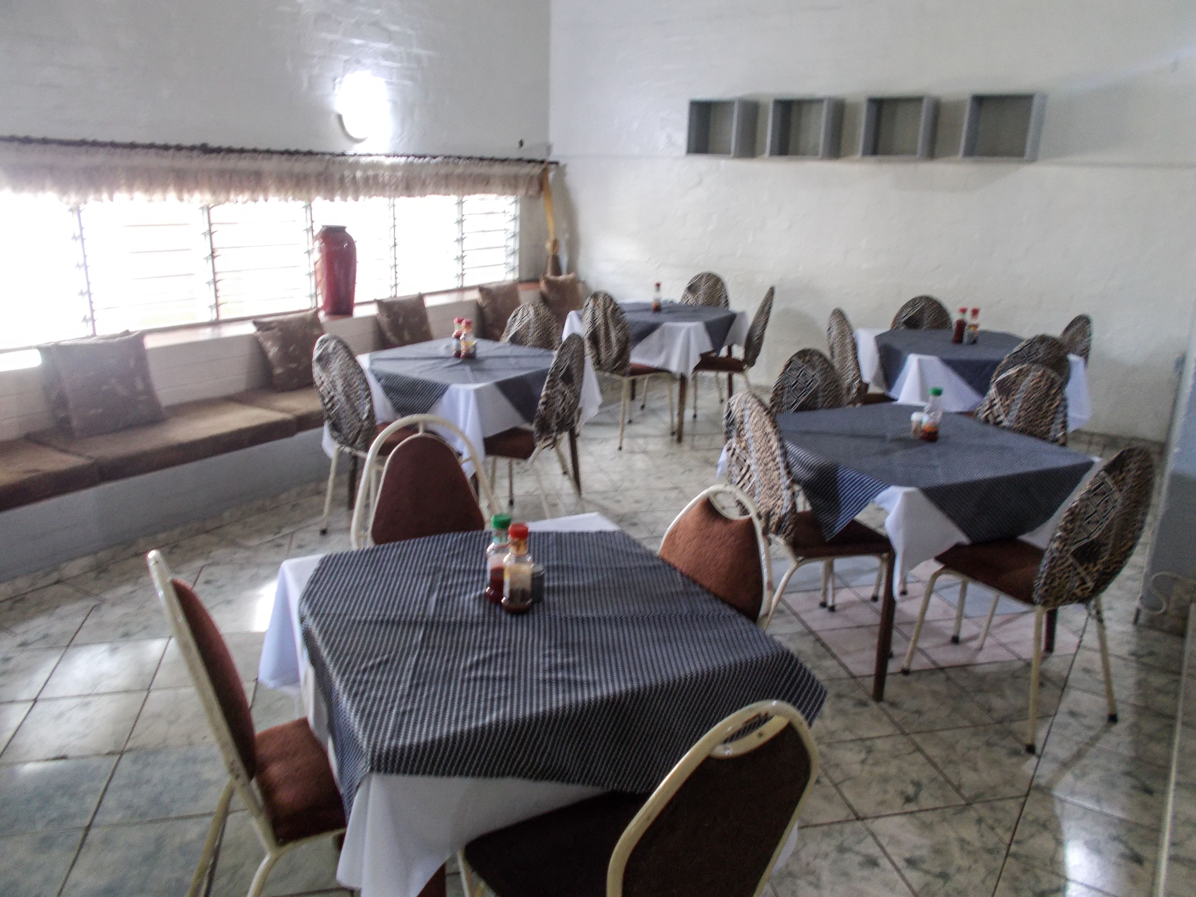 Uma área de refeições com mesas e cadeiras, uma janela com persianas e um chão ladrilhado.
