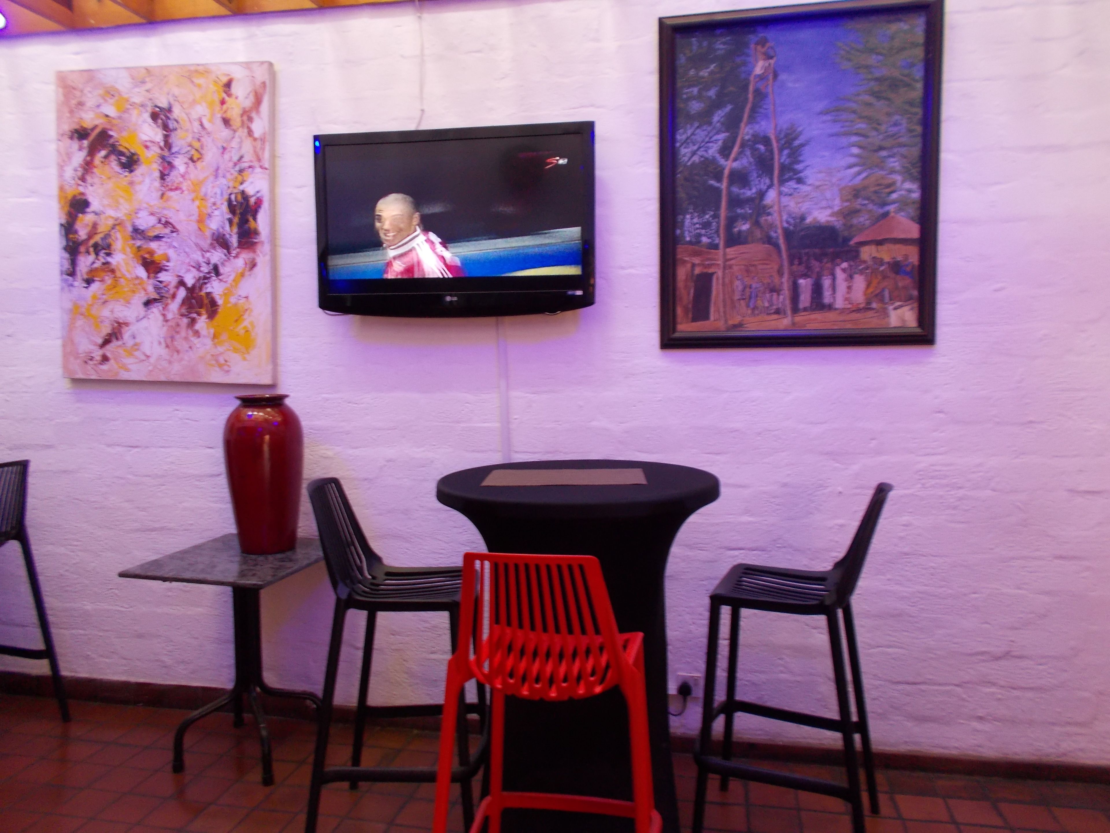 A room with a TV mounted on the wall, a table with chairs, and two paintings.