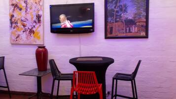 A room with a TV mounted on the wall, a table with chairs, and two paintings.