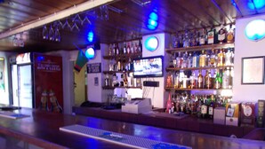 Un bar con mostrador, estantes llenos de botellas de licor y una pantalla de televisión.