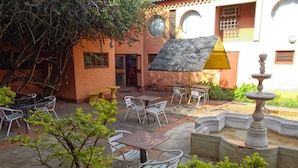 Un patio al aire libre con mesas y sillas, una fuente y un edificio con techo de tejas y ventanas.