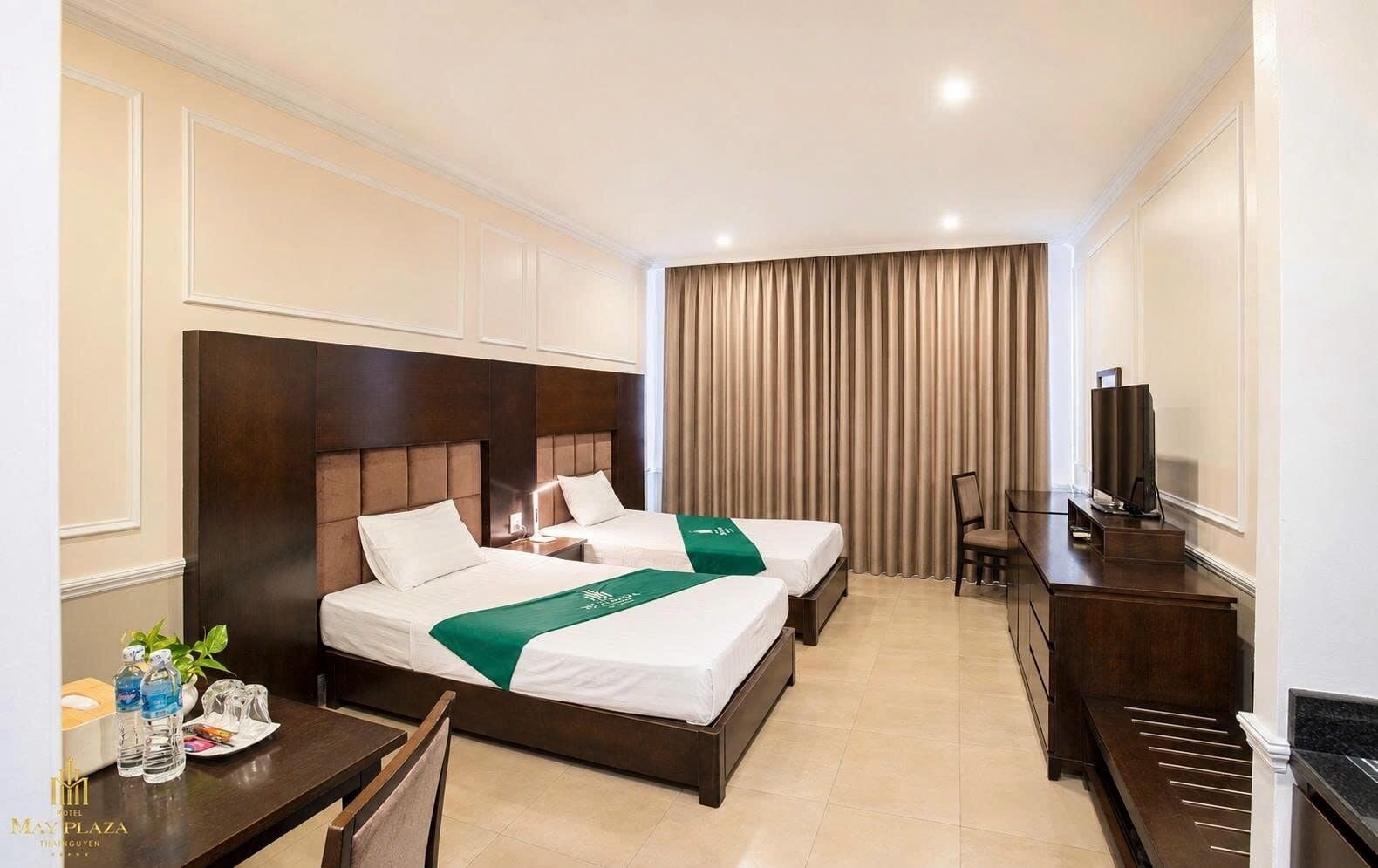 A hotel room with two beds, a desk, a chair, a television, and a curtain.