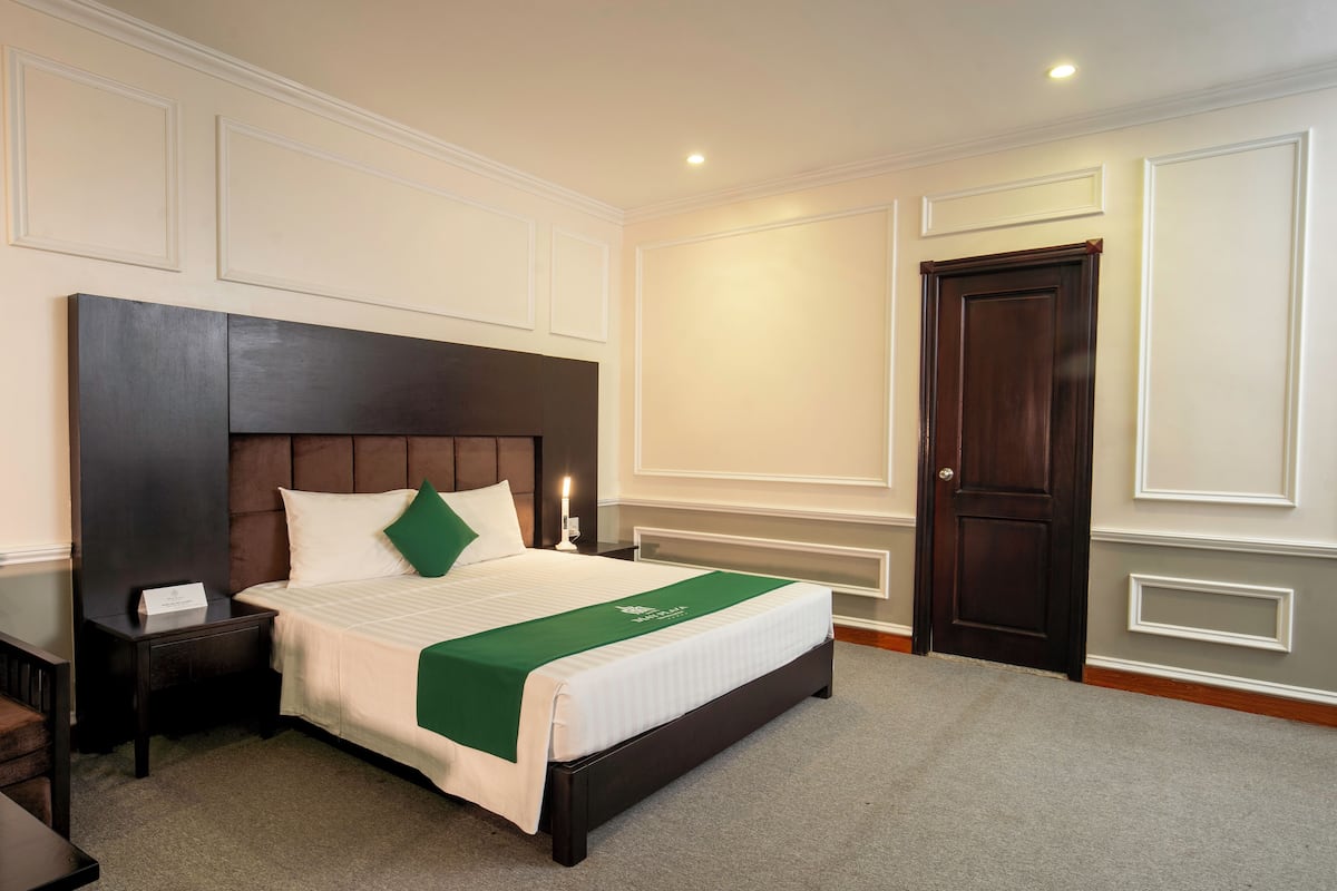 A neatly made bed with a green bedspread, a dark headboard, and a bedside table with a lamp.