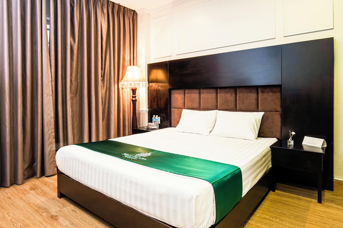 A hotel room with a large bed, a nightstand with a lamp, and a view of the outside through the curtains.